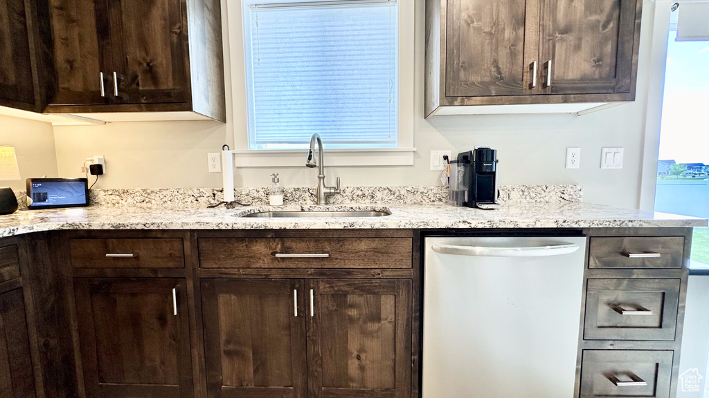 Kitchen featuring dishwasher, a sink, dark brown cabinets, and light stone counters