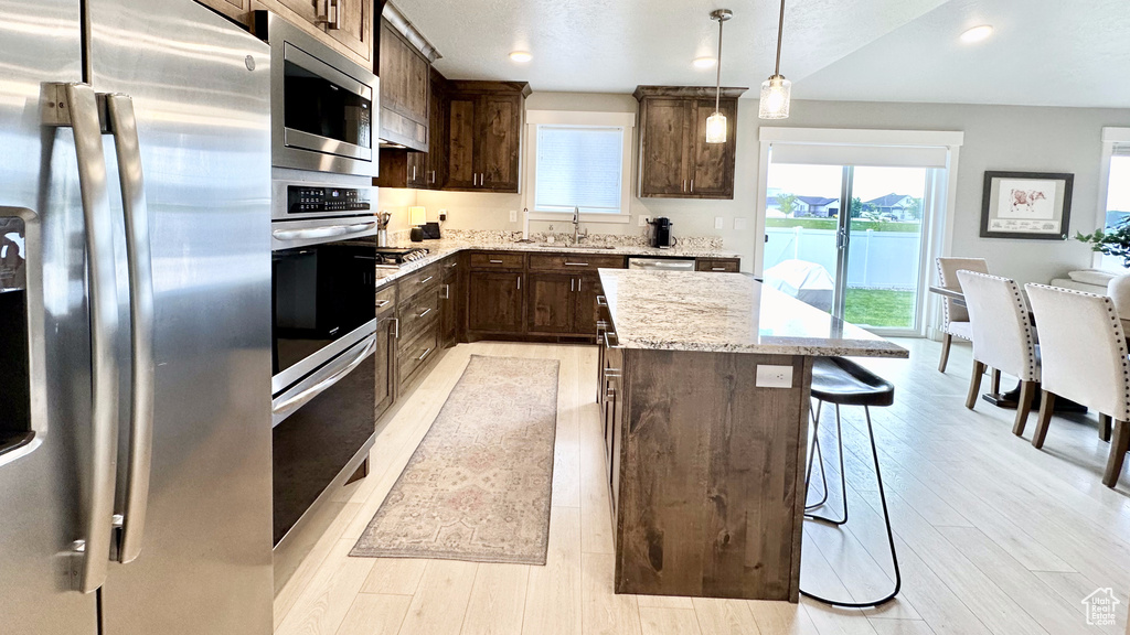 Kitchen featuring stainless steel appliances, a sink, dark brown cabinets, a kitchen bar, and a center island