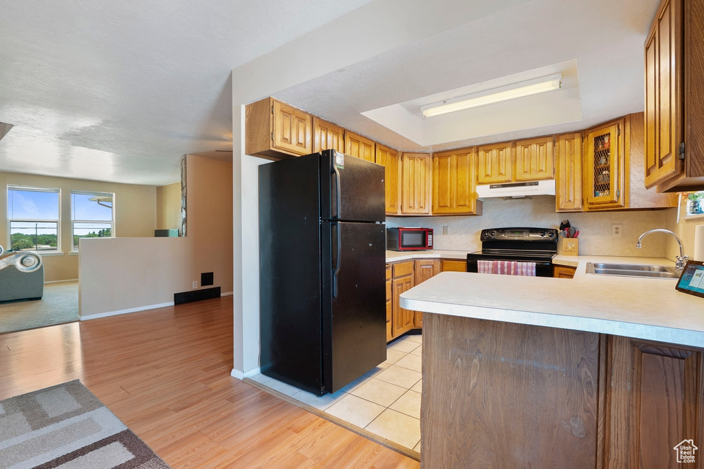Kitchen featuring black appliances, under cabinet range hood, a sink, light countertops, and a peninsula