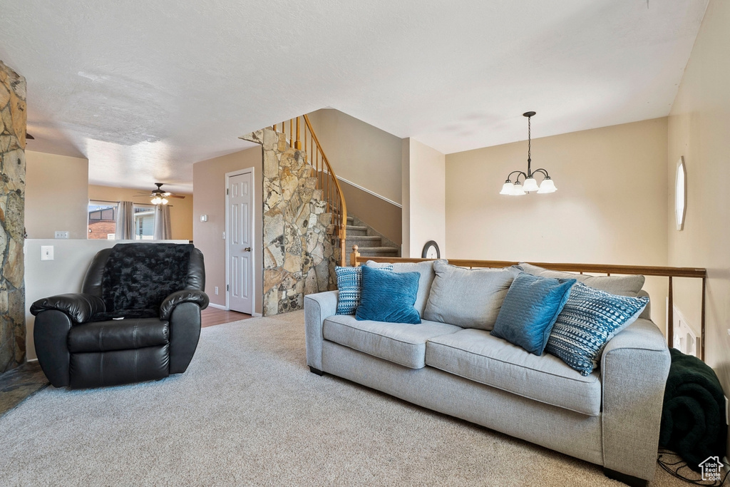 Carpeted living area with a chandelier, stairway, and a ceiling fan