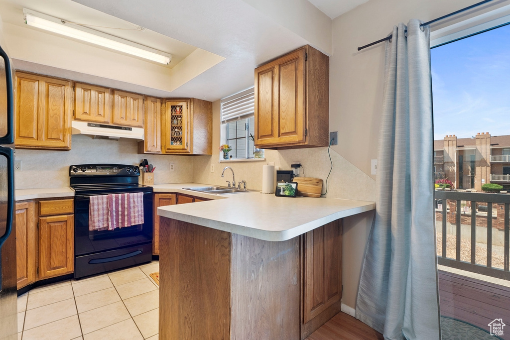 Kitchen featuring electric range, under cabinet range hood, a sink, a peninsula, and light countertops
