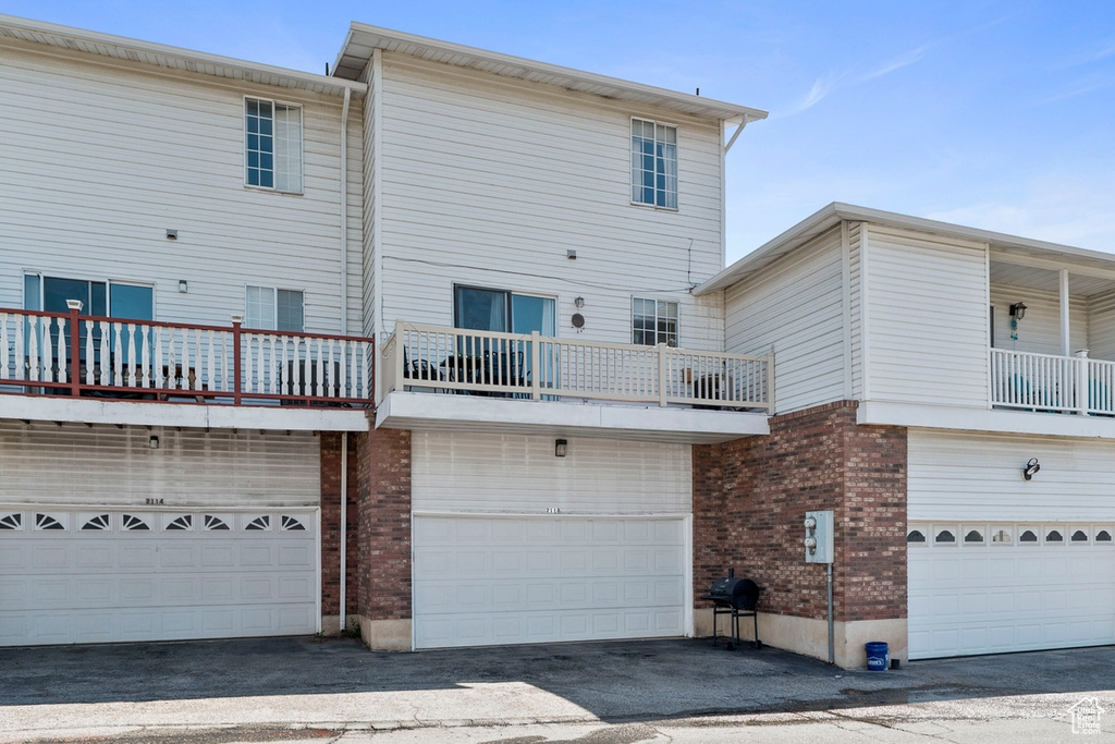Rear view of property featuring an attached garage, brick siding, a balcony, and driveway