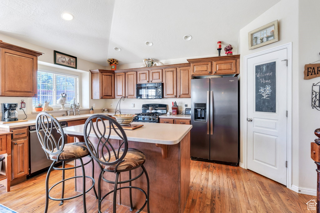 Kitchen featuring appliances with stainless steel finishes, a kitchen island, brown cabinetry, light countertops, and recessed lighting