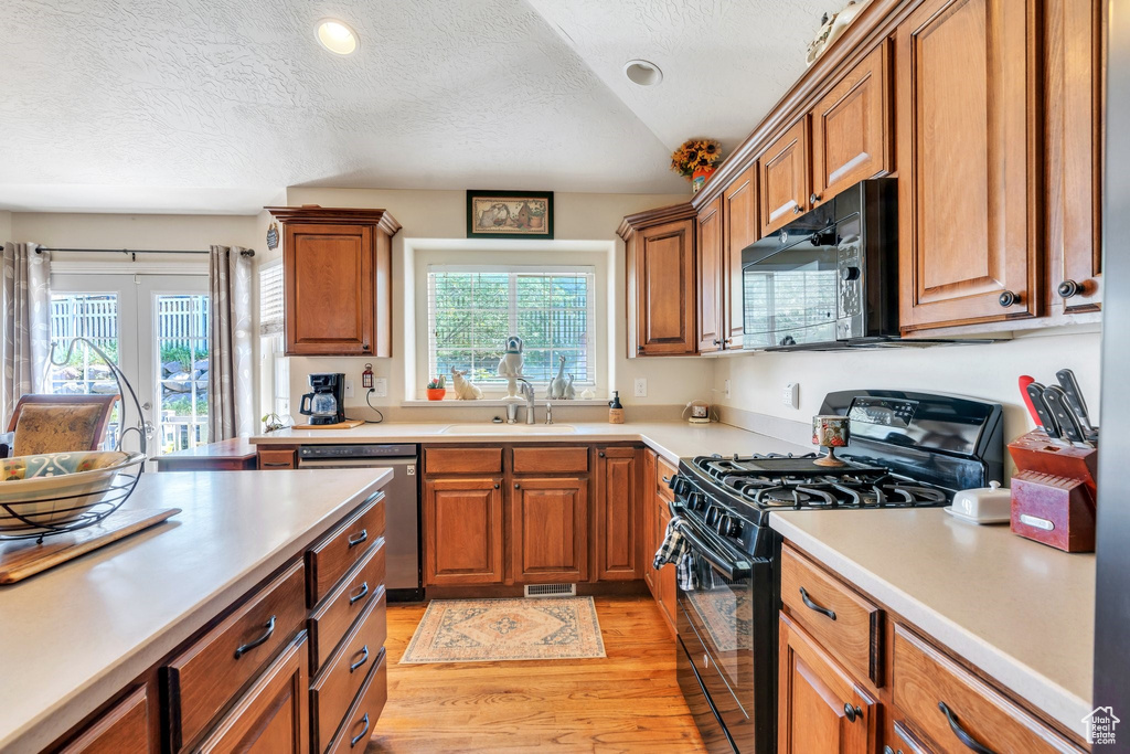 Kitchen with black appliances, a sink, light wood-type flooring, brown cabinets, and light countertops