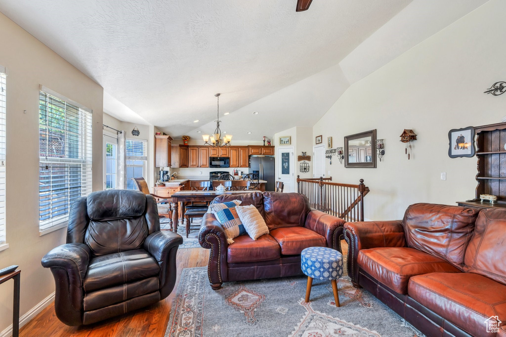 Living area featuring a chandelier, wood finished floors, vaulted ceiling, and baseboards
