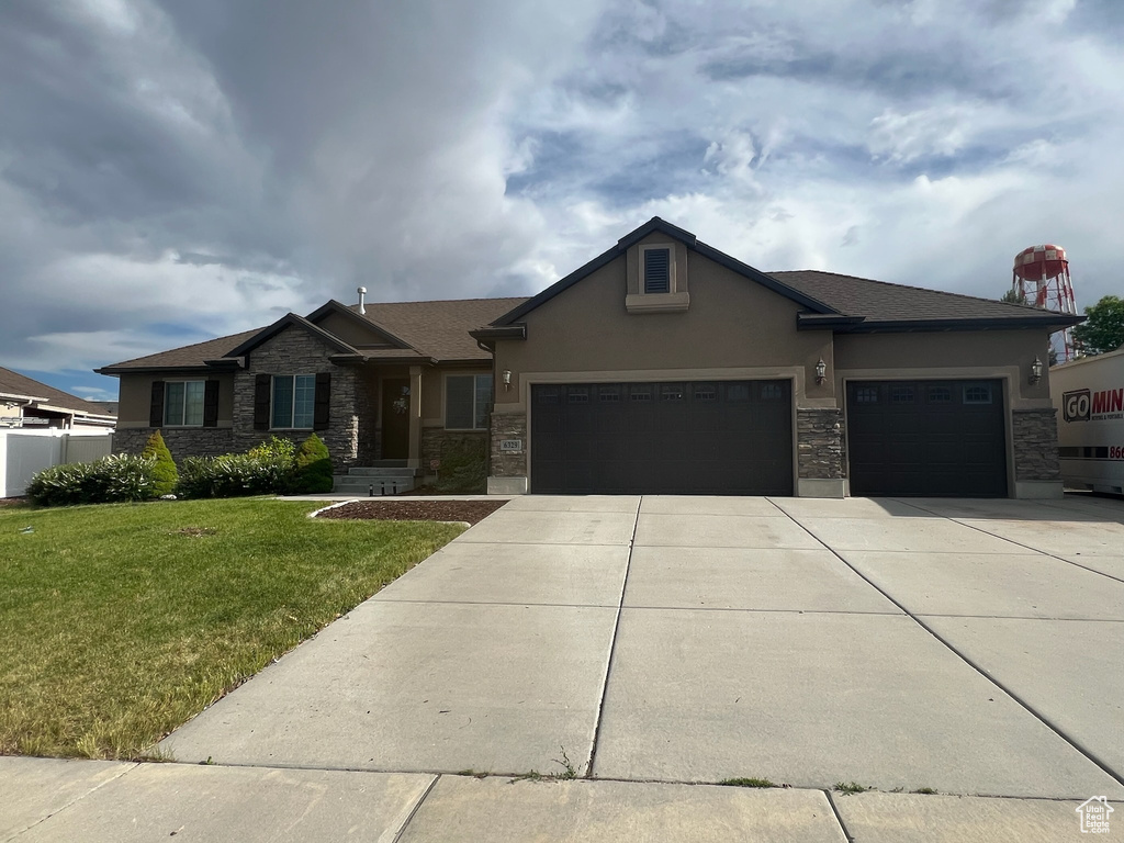 View of front of property featuring an attached garage, a front lawn, stucco siding, and stone siding