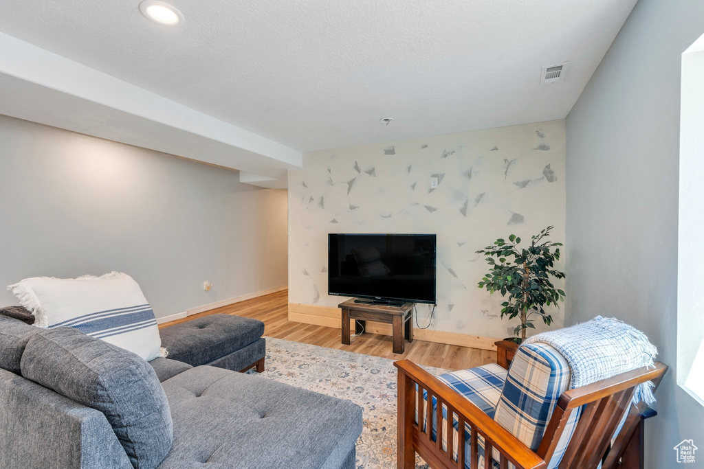 Living room with wood finished floors, baseboards, an accent wall, and recessed lighting