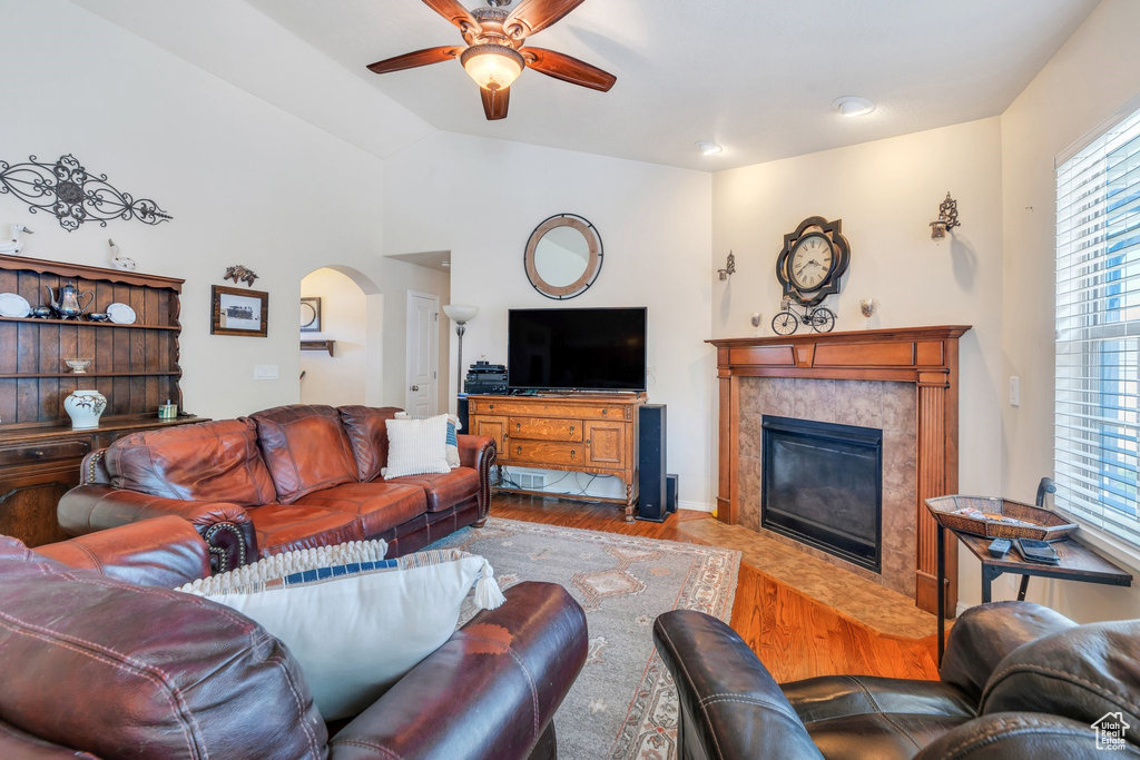 Living room featuring ceiling fan, arched walkways, wood finished floors, a premium fireplace, and vaulted ceiling