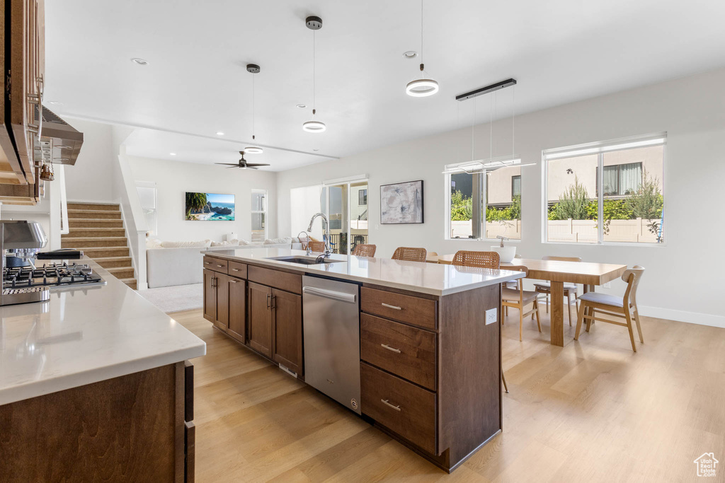 Kitchen with stainless steel appliances, a sink, light wood-style flooring, light countertops, and a center island with sink