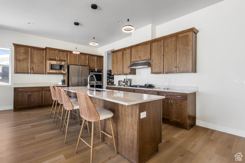 Kitchen with appliances with stainless steel finishes, a sink, light wood finished floors, and baseboards