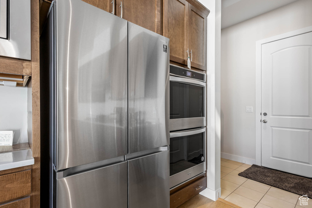 Kitchen featuring stainless steel appliances, light tile patterned floors, brown cabinets, light countertops, and baseboards