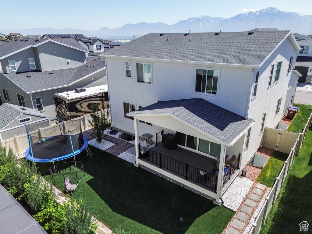 Rear view of house with a mountain view, a trampoline, stucco siding, roof with shingles, and a patio