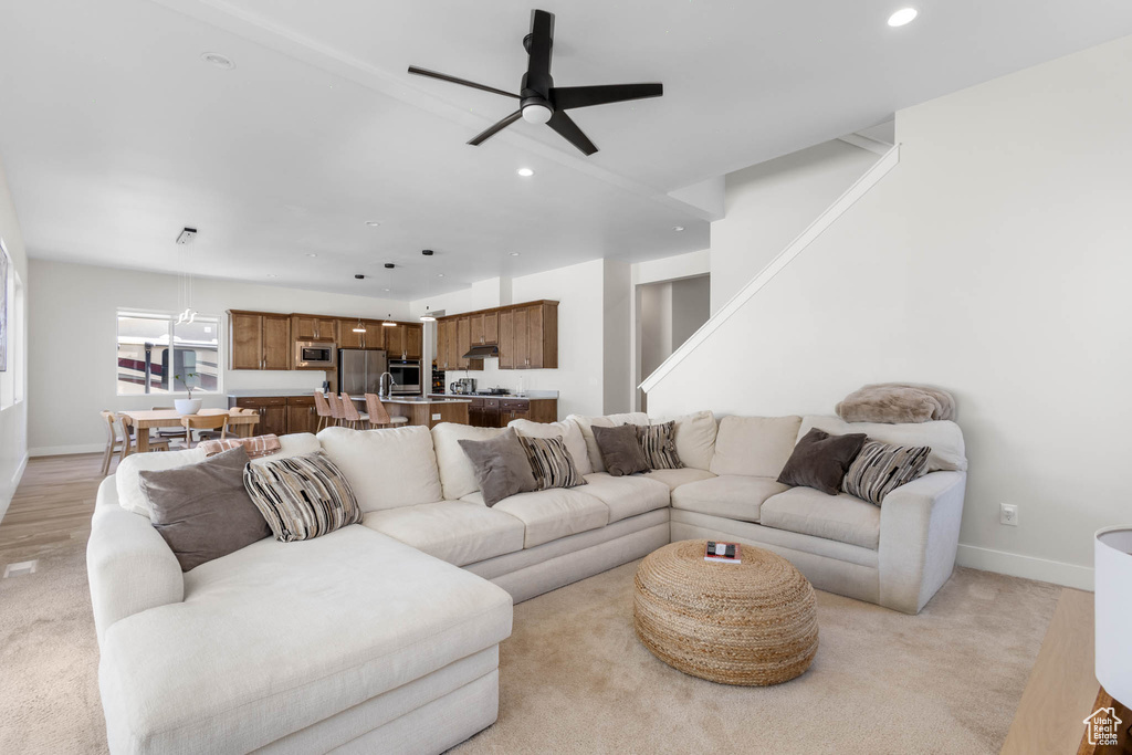 Living room featuring ceiling fan, recessed lighting, baseboards, light colored carpet, and stairs