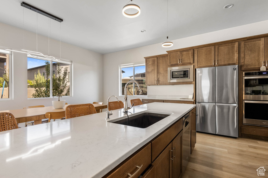Kitchen with stainless steel appliances, a sink, light wood finished floors, light stone counters, and recessed lighting