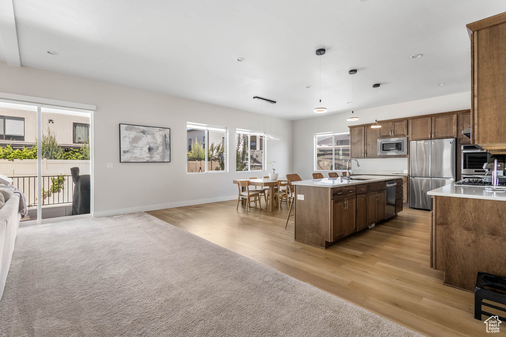Kitchen with appliances with stainless steel finishes, open floor plan, light countertops, a center island with sink, and light wood-style flooring