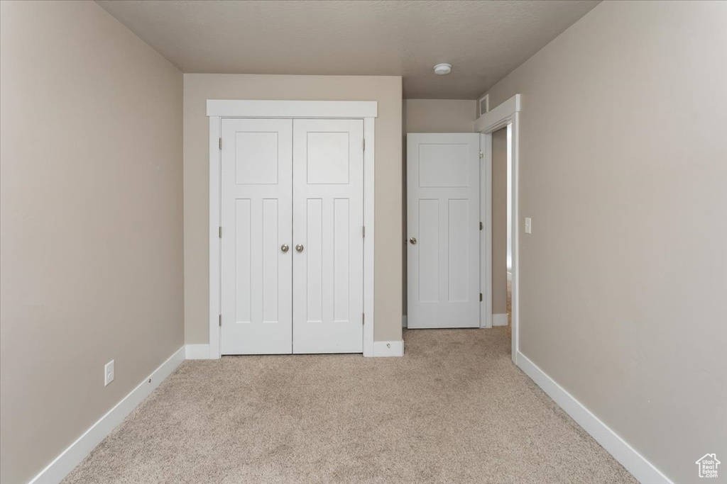 Unfurnished bedroom featuring light colored carpet, baseboards, and a closet