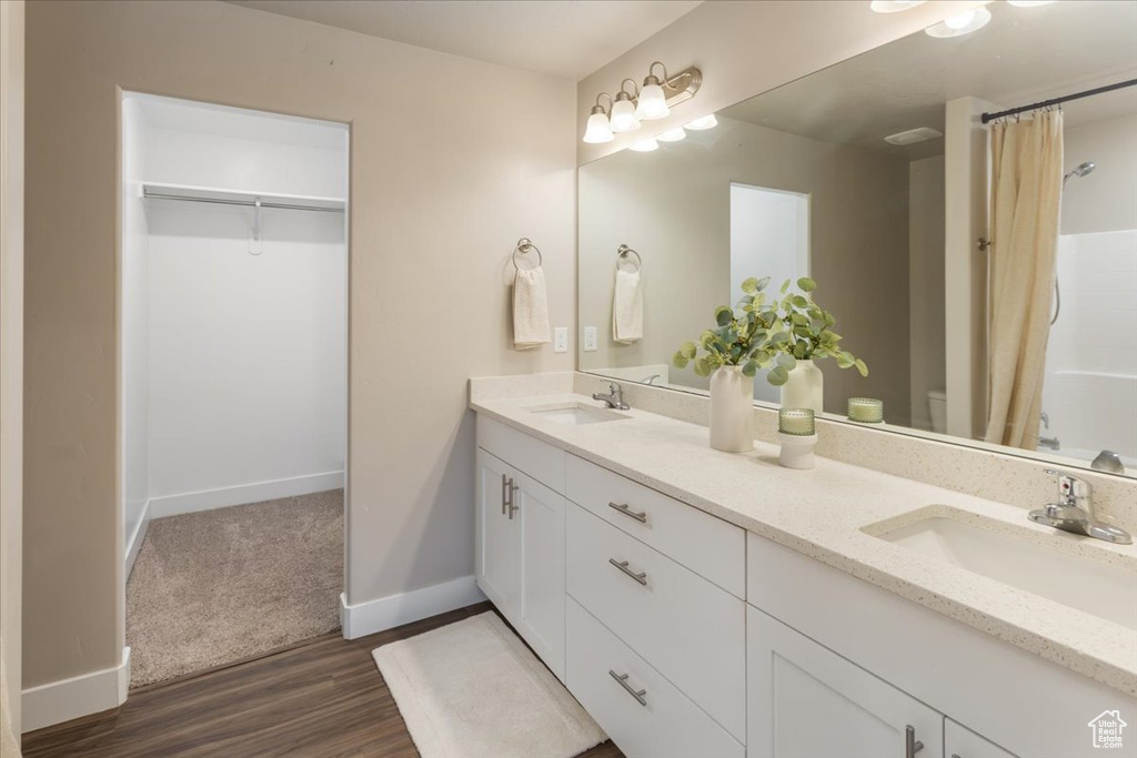 Bathroom featuring double vanity, wood finished floors, baseboards, a shower with shower curtain, and a spacious closet