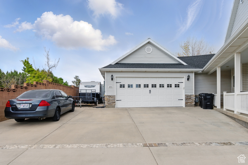 View of side of home with stone siding, a shingled roof, concrete driveway, and an attached garage