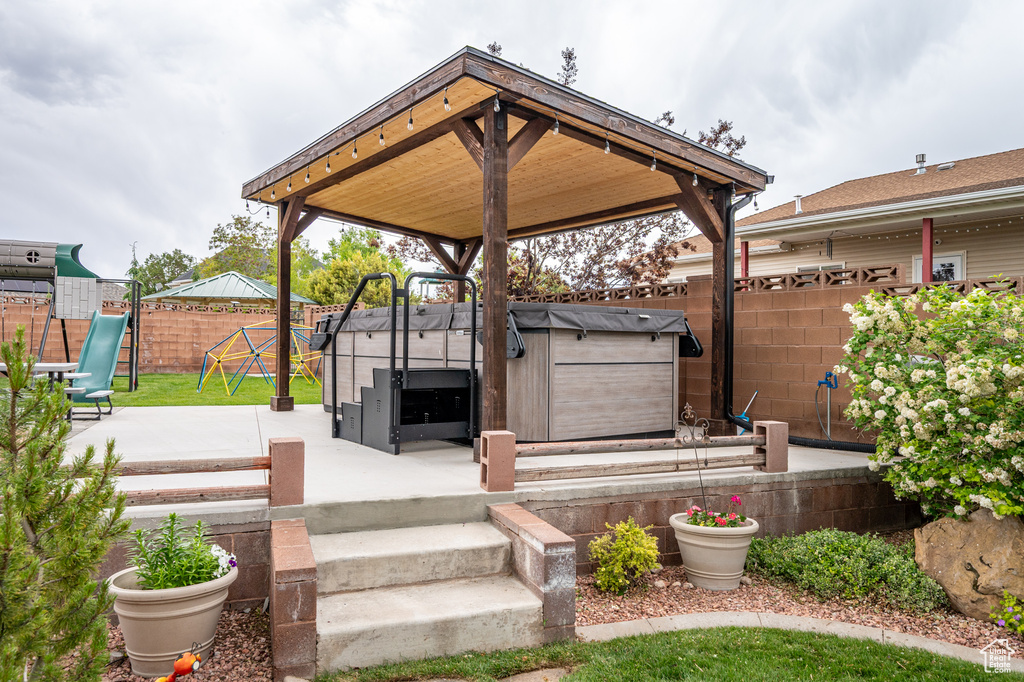 Fenced backyard featuring a patio, a playground, a gazebo, and a hot tub