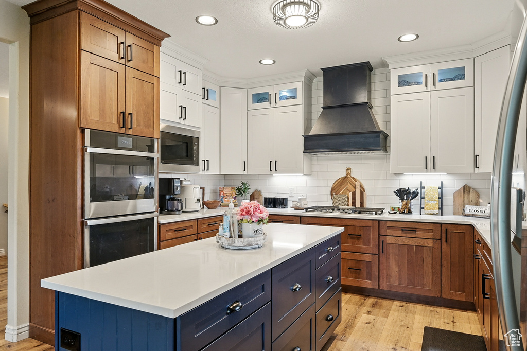 Kitchen with premium range hood, appliances with stainless steel finishes, light wood finished floors, light countertops, and recessed lighting