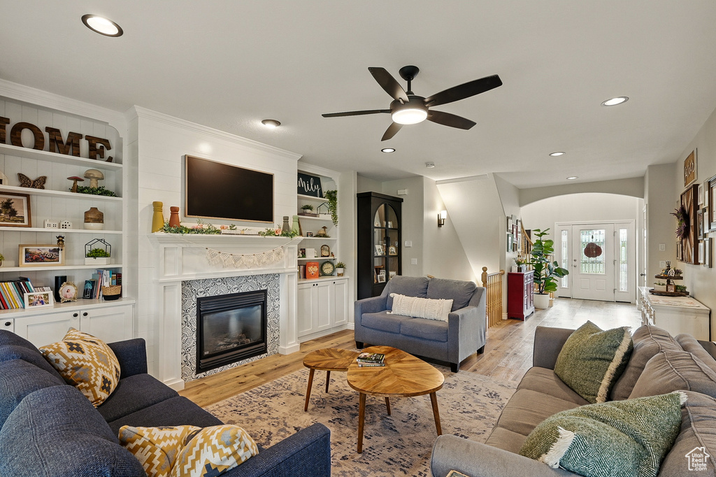 Living room featuring a ceiling fan, light wood finished floors, arched walkways, recessed lighting, and a glass covered fireplace