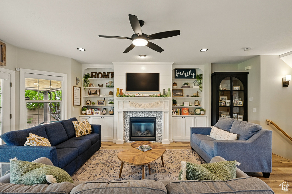 Living room with light wood-type flooring, a ceiling fan, a tile fireplace, recessed lighting, and built in features