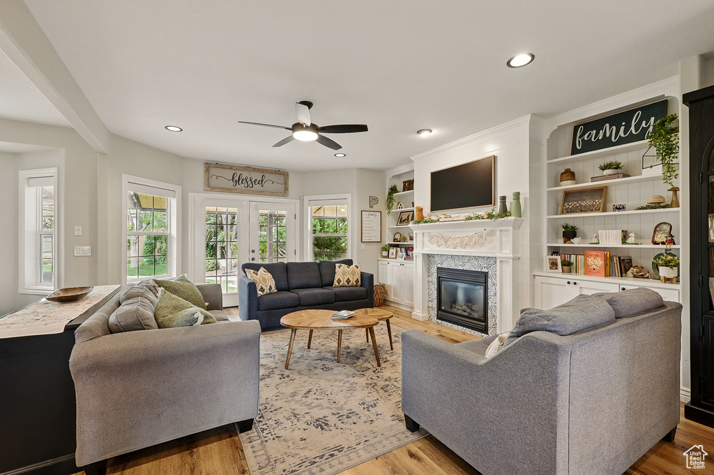 Living area with a ceiling fan, a glass covered fireplace, wood finished floors, healthy amount of natural light, and recessed lighting
