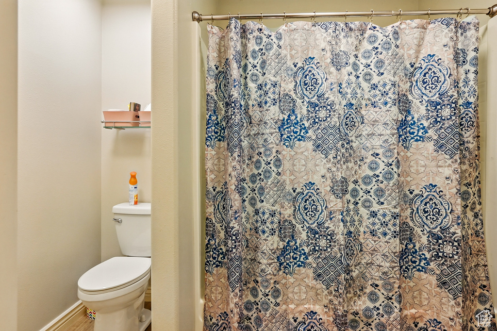 Bathroom featuring toilet, curtained shower, and wood finished floors
