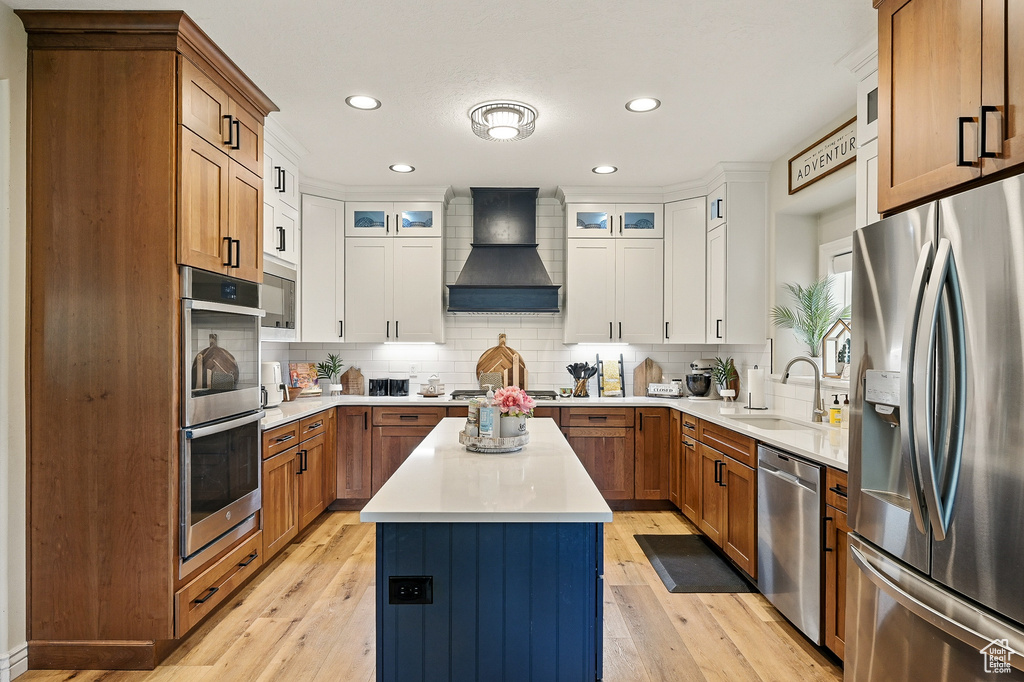 Kitchen with stainless steel appliances, custom exhaust hood, a sink, backsplash, and a kitchen island