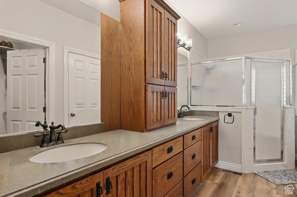 Full bath featuring a shower stall, double vanity, and wood finished floors