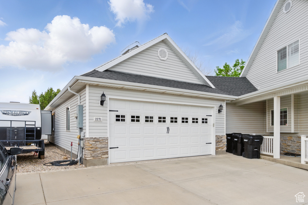 View of front facade featuring driveway, stone siding, a garage, and roof with shingles