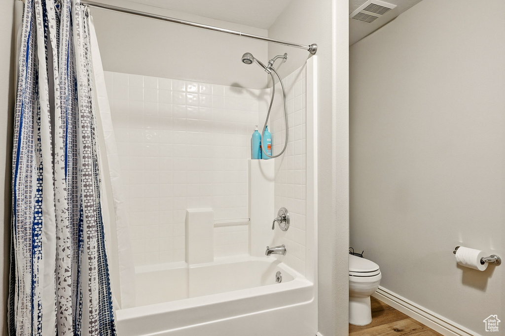 Full bath with shower / bath combo with shower curtain, toilet, wood finished floors, and baseboards