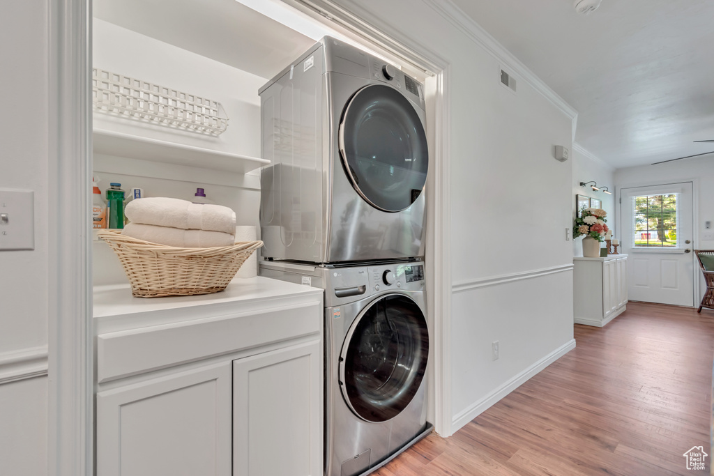 Laundry room with stacked washing machine and dryer, light wood-type flooring, crown molding, baseboards, and cabinet space