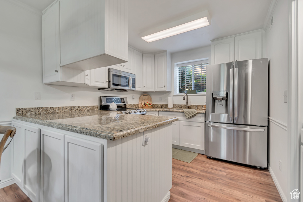 Kitchen with stainless steel appliances, white cabinetry, and light wood finished floors
