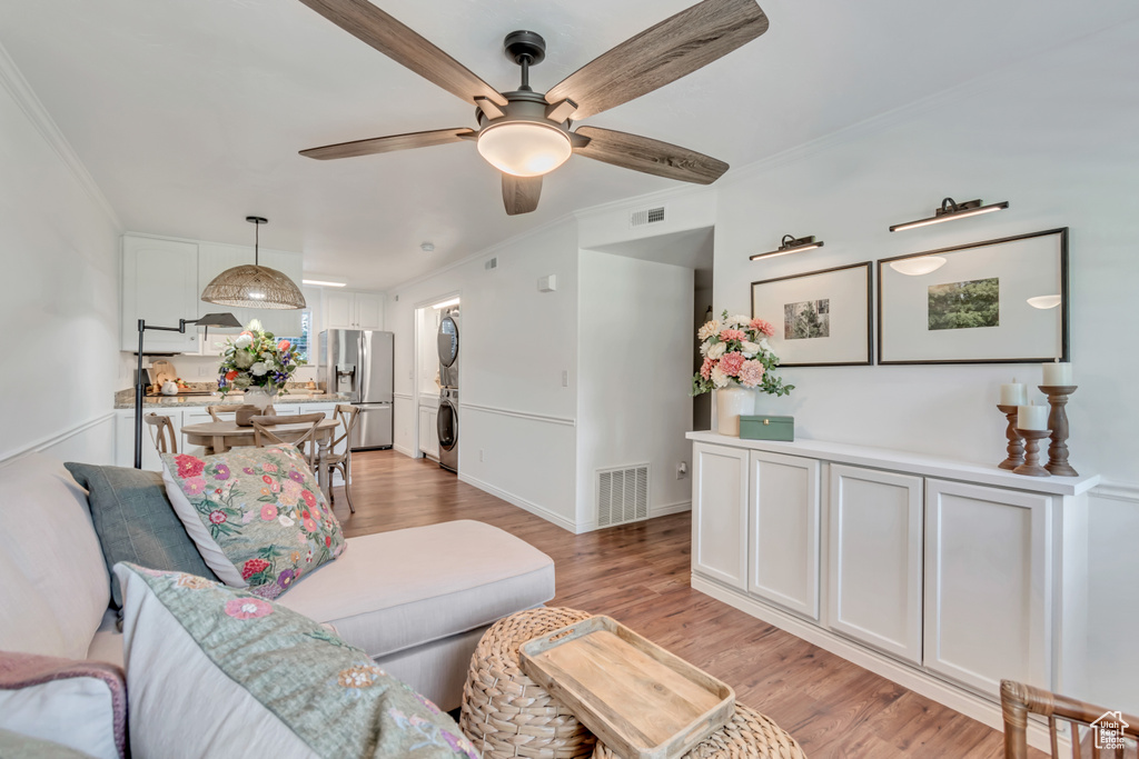 Living room featuring stacked washer / dryer, a ceiling fan, crown molding, and light wood finished floors