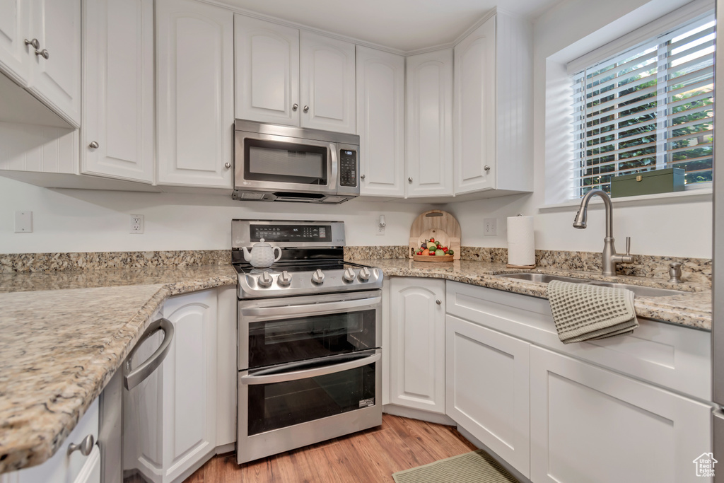 Kitchen with appliances with stainless steel finishes, a sink, white cabinetry, and light wood-style floors