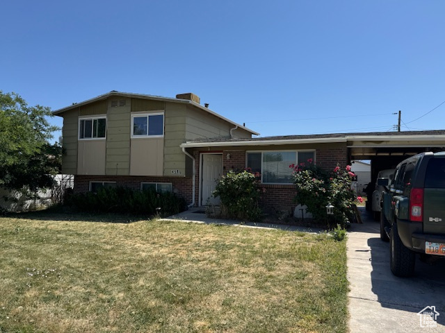 Split level home with brick siding, a front yard, and an attached carport