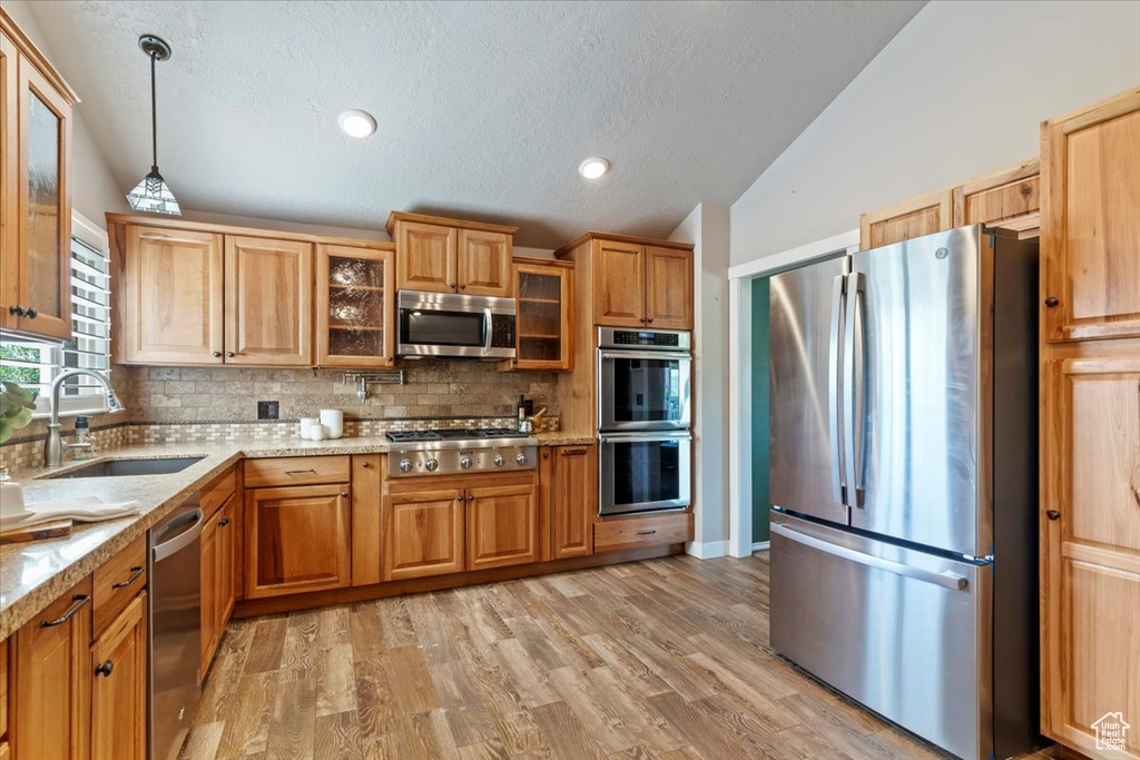 Kitchen with appliances with stainless steel finishes, a sink, vaulted ceiling, backsplash, and decorative light fixtures