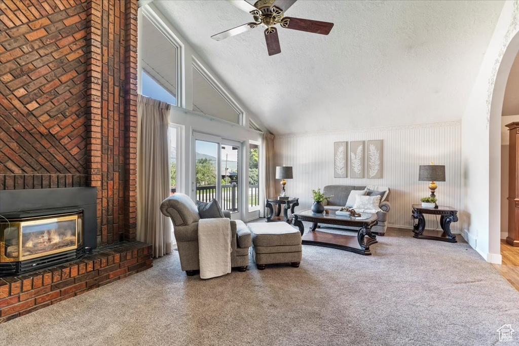 Carpeted living area featuring a ceiling fan, a textured ceiling, a brick fireplace, vaulted ceiling, and arched walkways