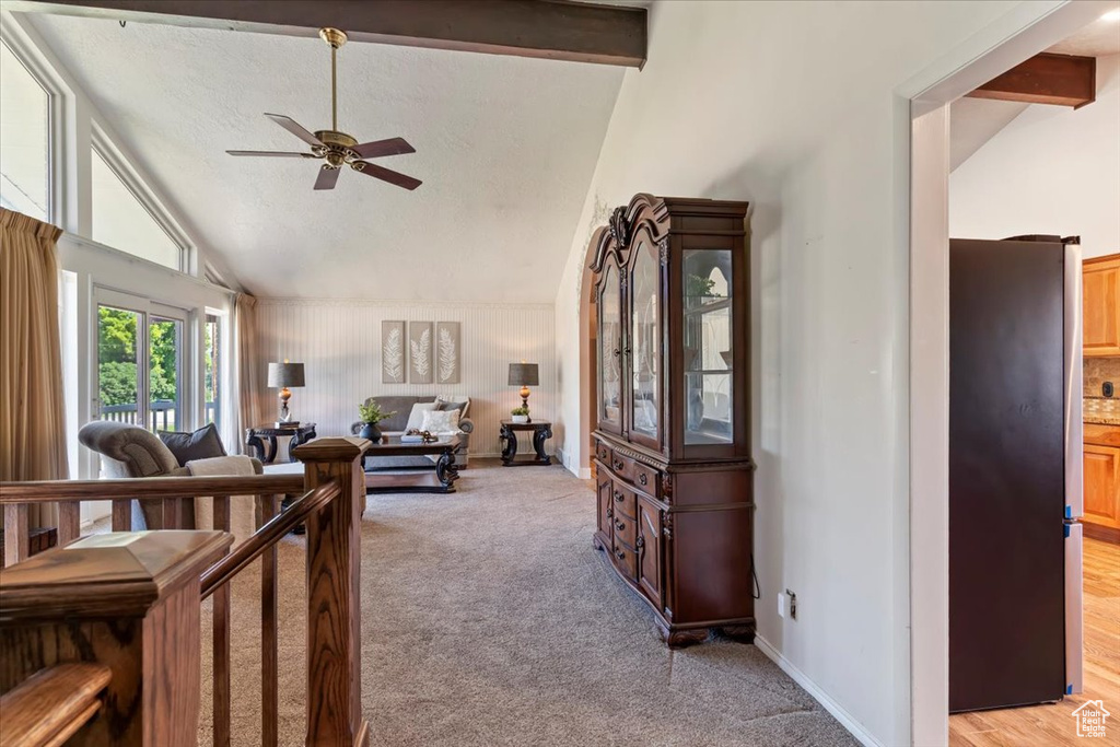 Living area with ceiling fan, light carpet, high vaulted ceiling, and beamed ceiling