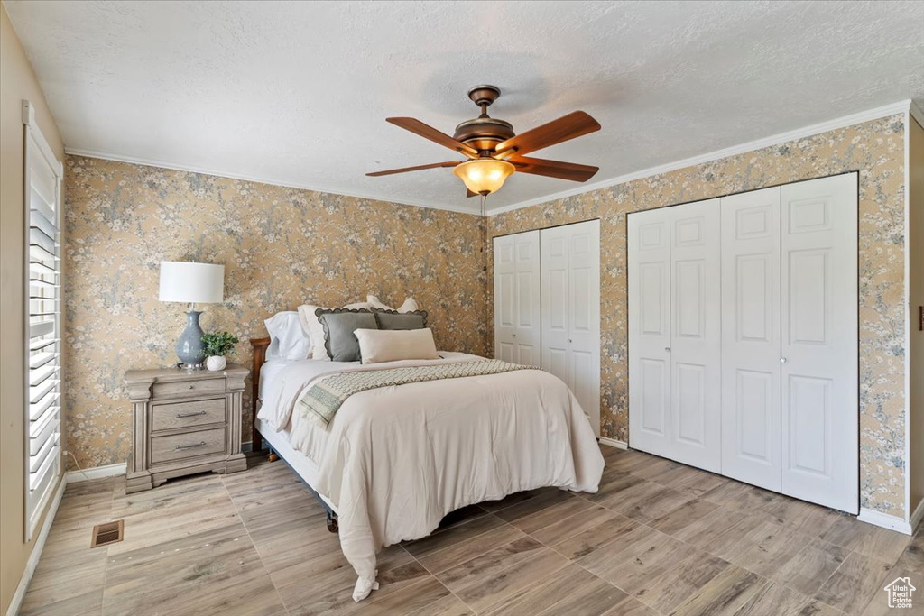 Bedroom with wallpapered walls, ornamental molding, multiple closets, a textured ceiling, and baseboards