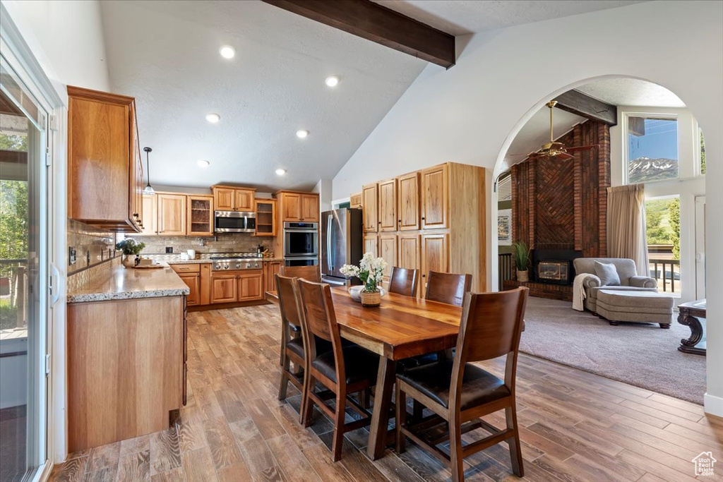 Dining room featuring beamed ceiling, arched walkways, high vaulted ceiling, a fireplace, and light wood-type flooring