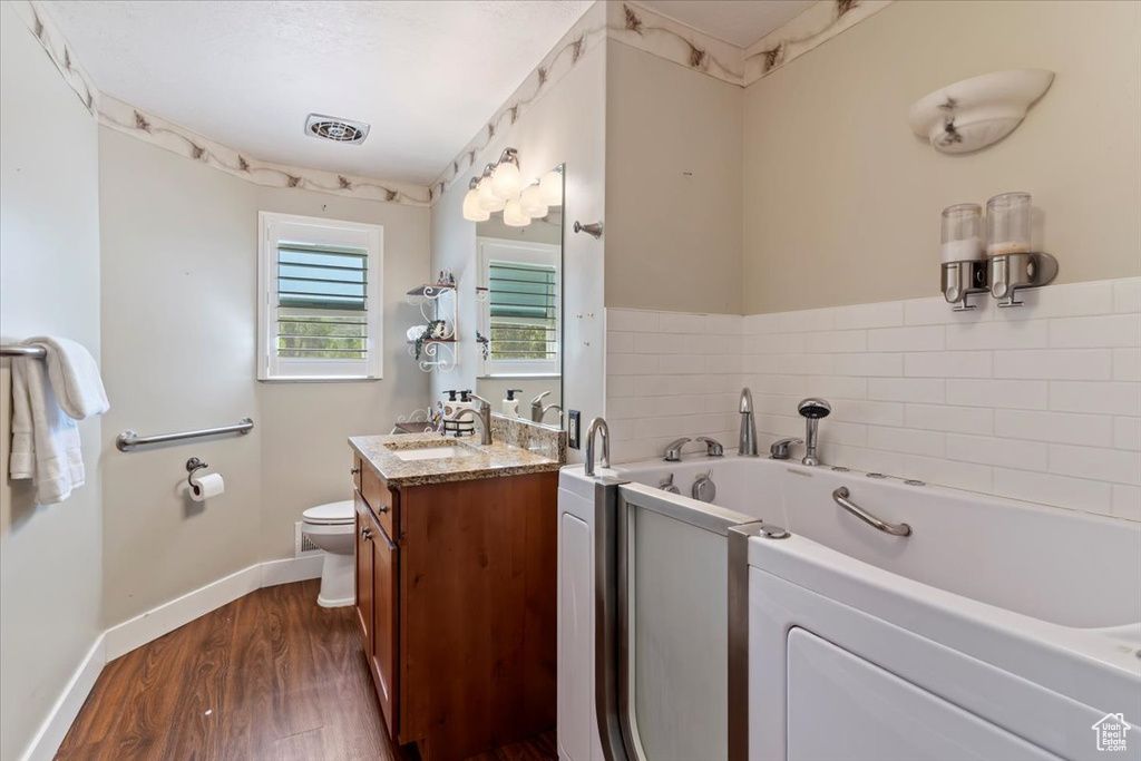 Full bathroom with vanity, toilet, a garden tub, wood finished floors, and baseboards