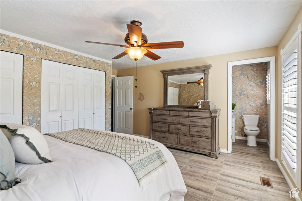 Bedroom featuring baseboards, ensuite bath, ceiling fan, and light wood-style floors