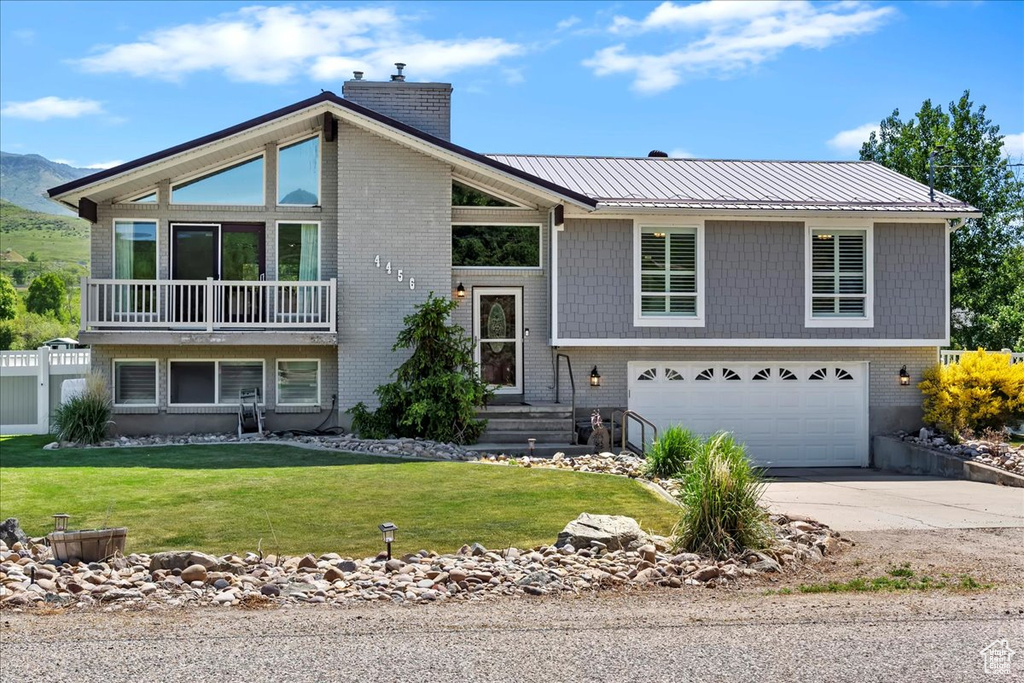 View of front of house with a garage, a chimney, concrete driveway, a front lawn, and metal roof