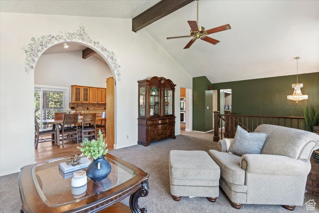 Carpeted living room with arched walkways, ceiling fan, a chandelier, high vaulted ceiling, and beamed ceiling