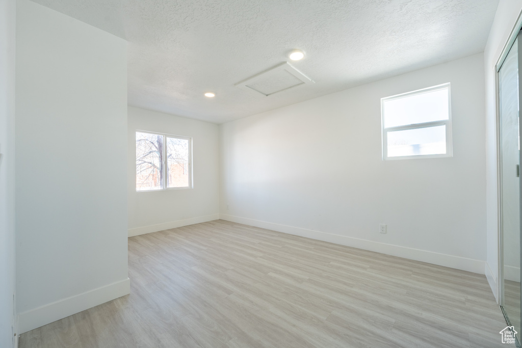 Empty room featuring attic access, baseboards, light wood-style flooring, recessed lighting, and a textured ceiling