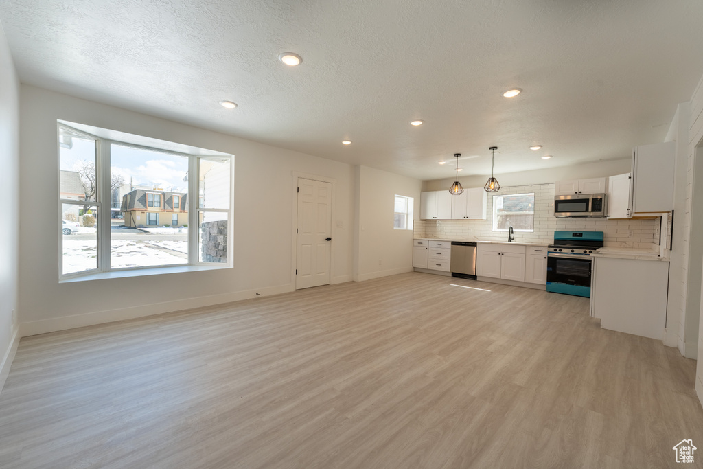 Unfurnished living room featuring light wood finished floors, baseboards, recessed lighting, and a sink