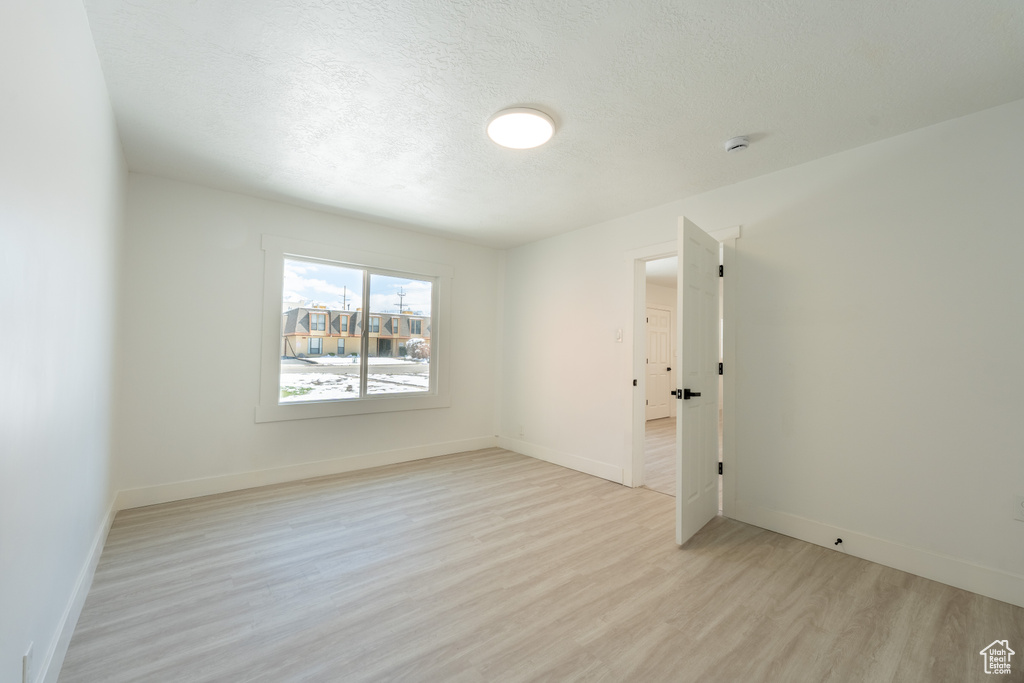 Spare room with light wood finished floors, a textured ceiling, and baseboards