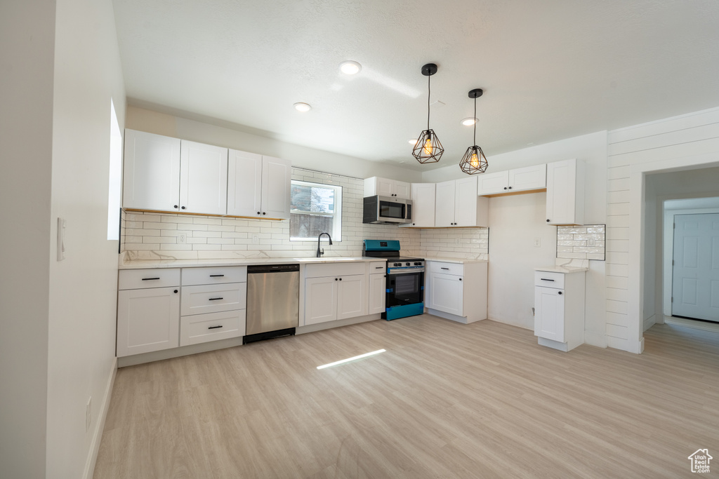 Kitchen with stainless steel appliances, a sink, light wood-style flooring, decorative backsplash, and white cabinetry